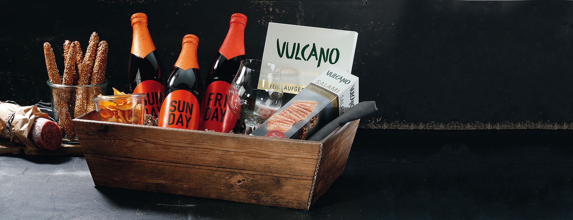 Square gift basket made of natural corrugated cardboard printed in a wood look with beer and salami.